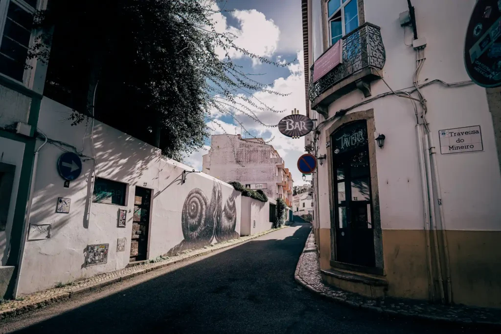 Rue pittoresque de Lagos, Portugal, avec fresques murales et ciel bleu partiellement nuageux.