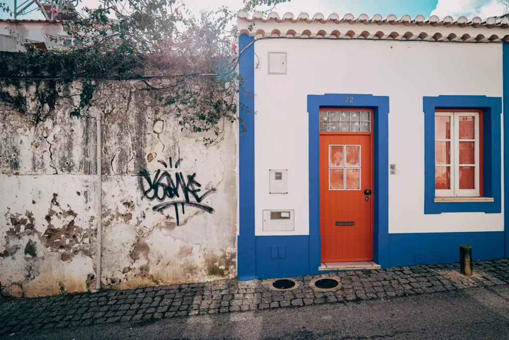 Façade colorée d'une maison traditionnelle à Lagos, Portugal, avec porte rouge et mur blanc orné de graffiti.
