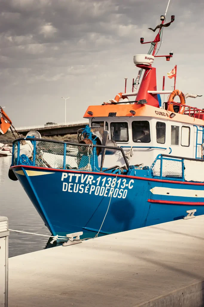 Bateau de pêche coloré amarré au port de Tavira, Algarve, sous un ciel nuageux.