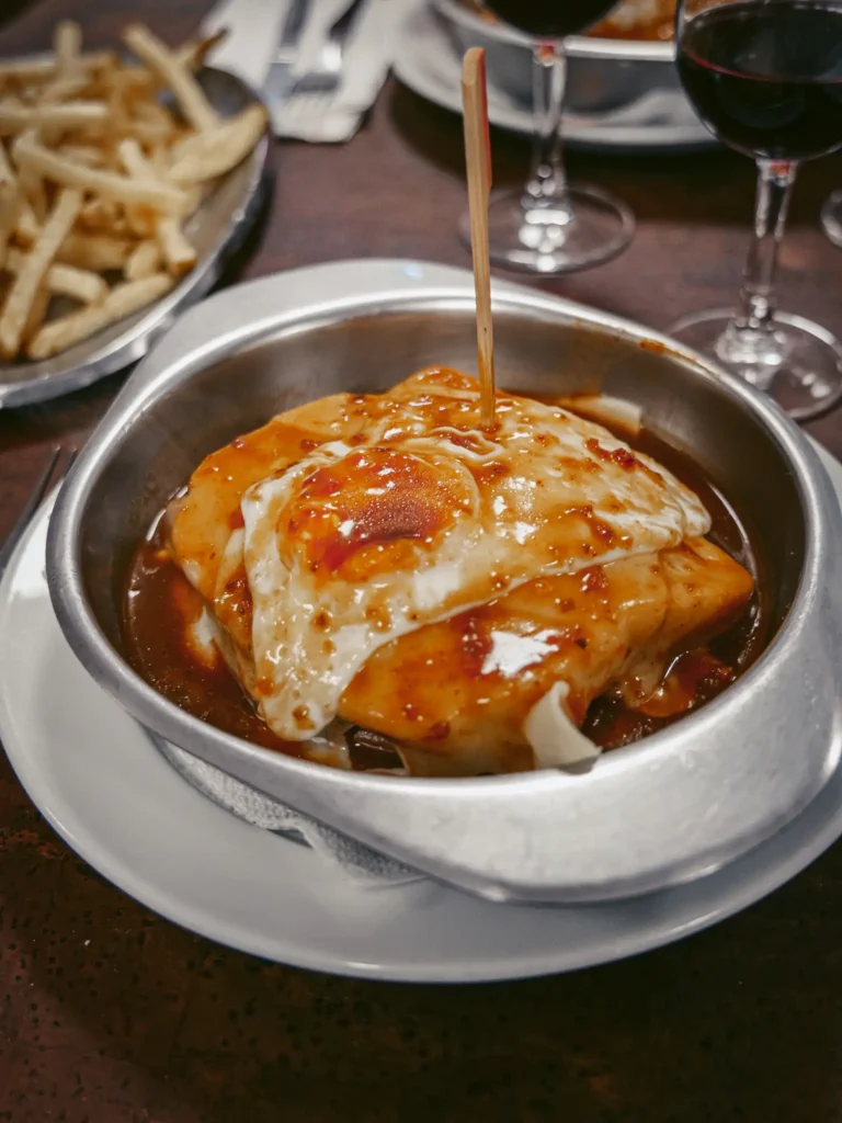 Francesinha served in a restaurant in Tomar, accompanied by fries and glasses of red wine.