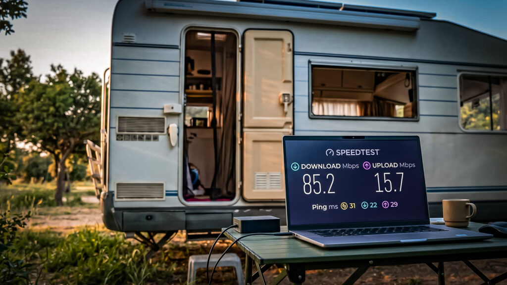 Outdoor caravan with computer displaying Starlink speed test, trees in the background.