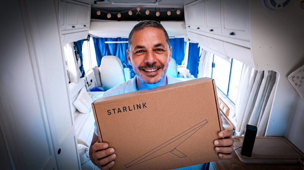 Xavier smiling holding a Starlink box in a converted camper van.