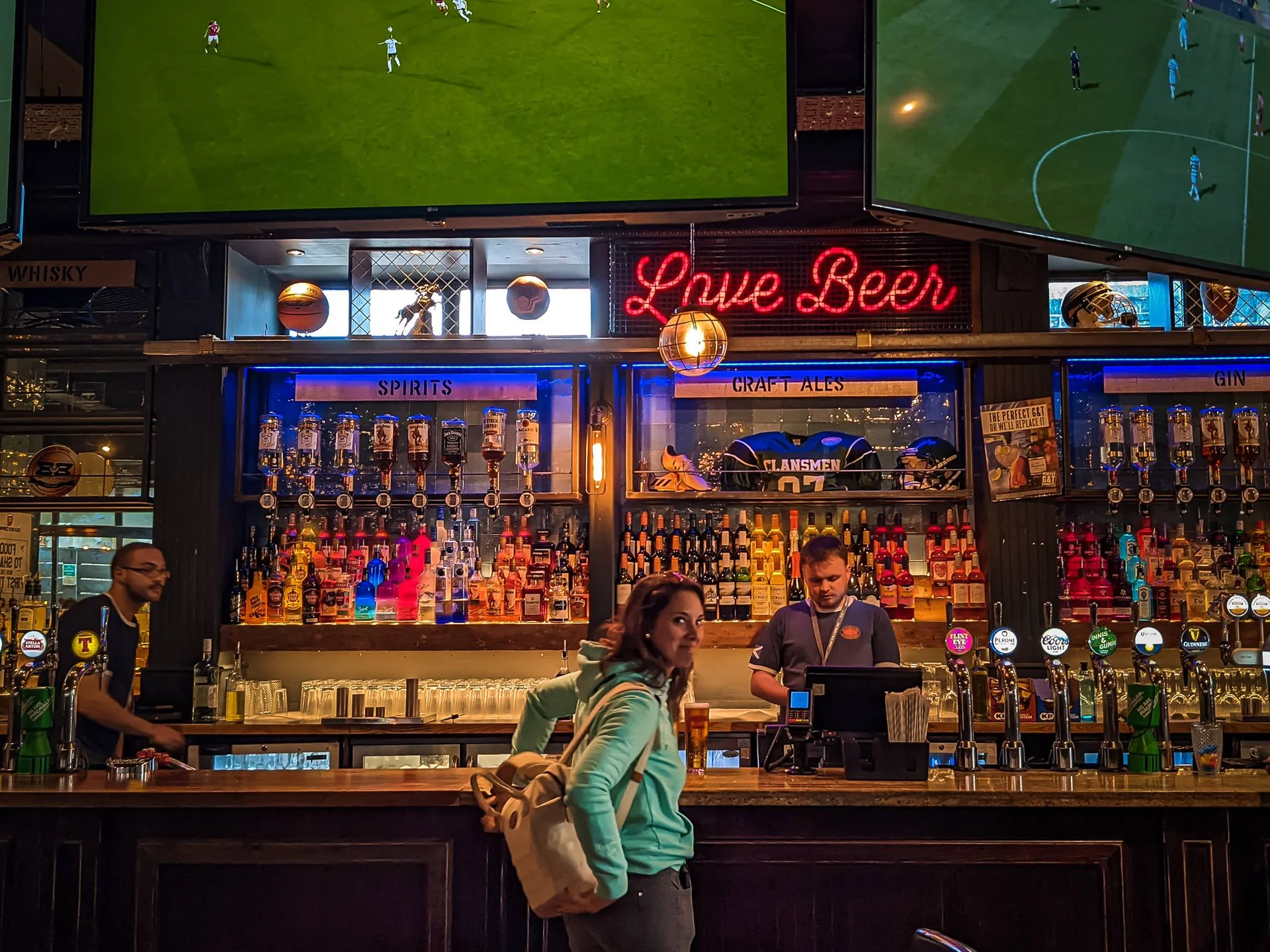 Caroline at the bar of a lively pub in Stirling with screens showing football matches
