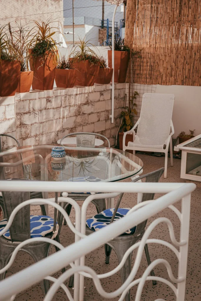 Sunny terrace in Fuseta, Algarve, with a glass table, metal chairs, and plant pots lined up on a low wall.