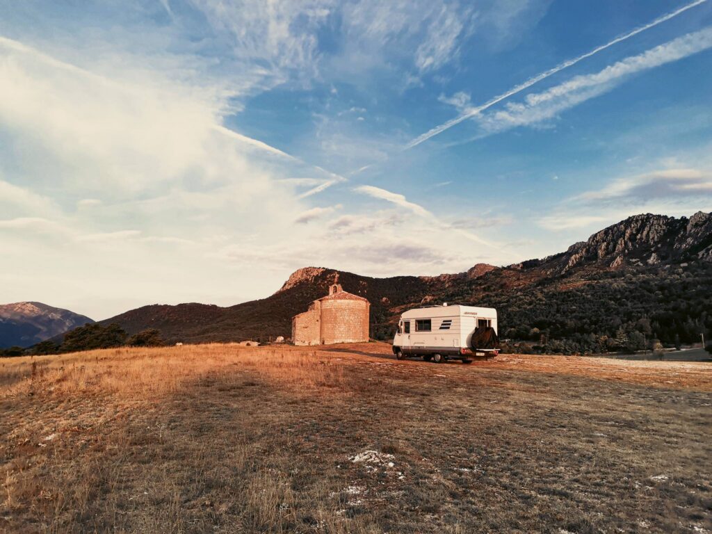 Camper Edouard is parked in front of a stone chapel surrounded by mountains, a symbol of the mobility and tax flexibility of the nomad.