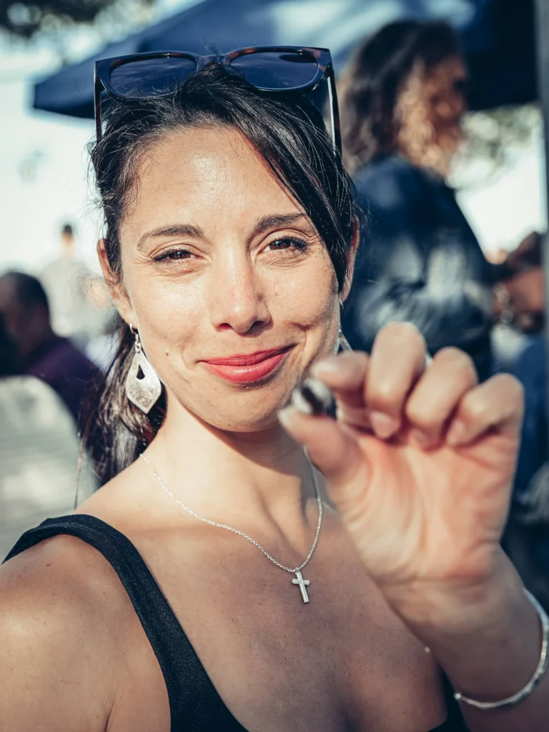 Caroline holds a snail between her fingers at an outdoor festival in Tavira, under natural light.