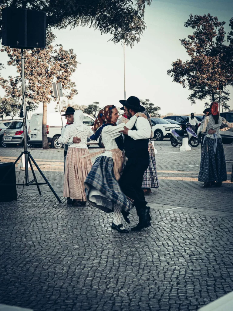 Couples in traditional Portuguese costumes dance outdoors in a cobbled square in Tavira during a festive event.