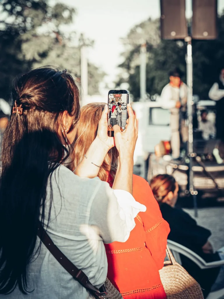 Caroline films the traditional dancers of a local caracois festival in Tavira Algarve, Portugal, where a stage is visible in the background.