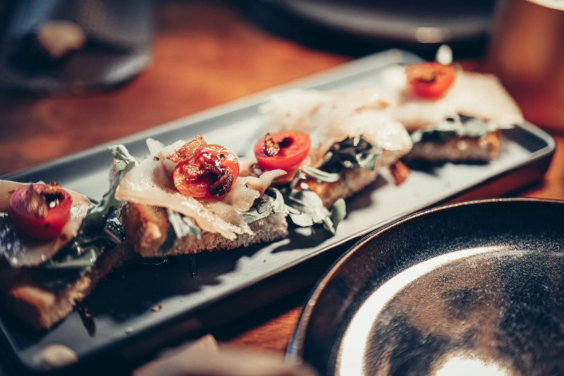 Plate of tapas made up of slices of bread topped with fresh vegetables and smoked cod, served on a wooden table at the 8 Tapas restaurant in Faro, Algarve.