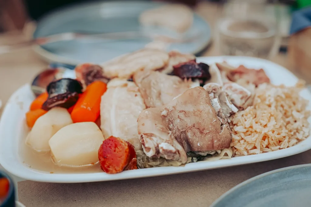 Plate of cozido à portuguesa served on a table, with pieces of meat, sausage, carrot, potato, and rice, in a restaurant in Portimao in the Algarve.