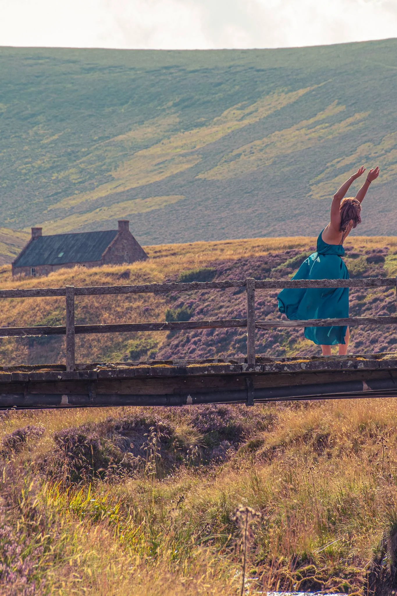 Caroline in a blue dress dances on a wooden bridge in the heart of the moors of Cairngorms National Park