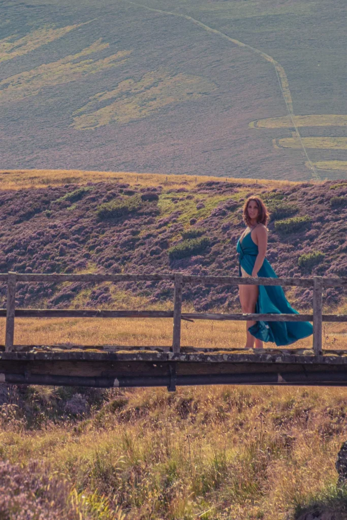 Caroline in a blue dress on a wooden bridge surrounded by moors and hills of the Cairngorms