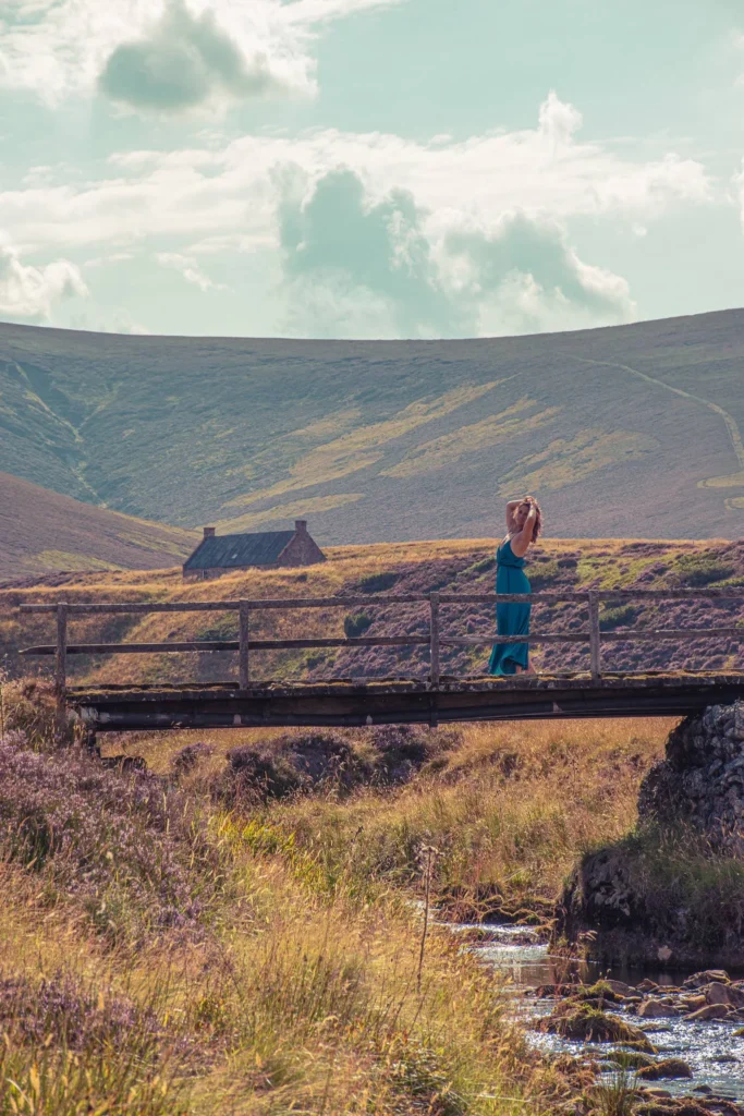 A woman in a turquoise dress on a wooden bridge over a stream in the Cairngorms