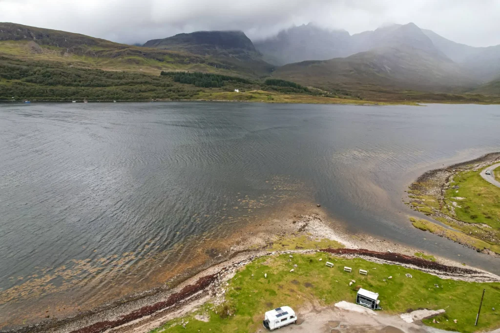 Aerial view of a loch on the Isle of Skye with a camper van parked by the water and misty mountains