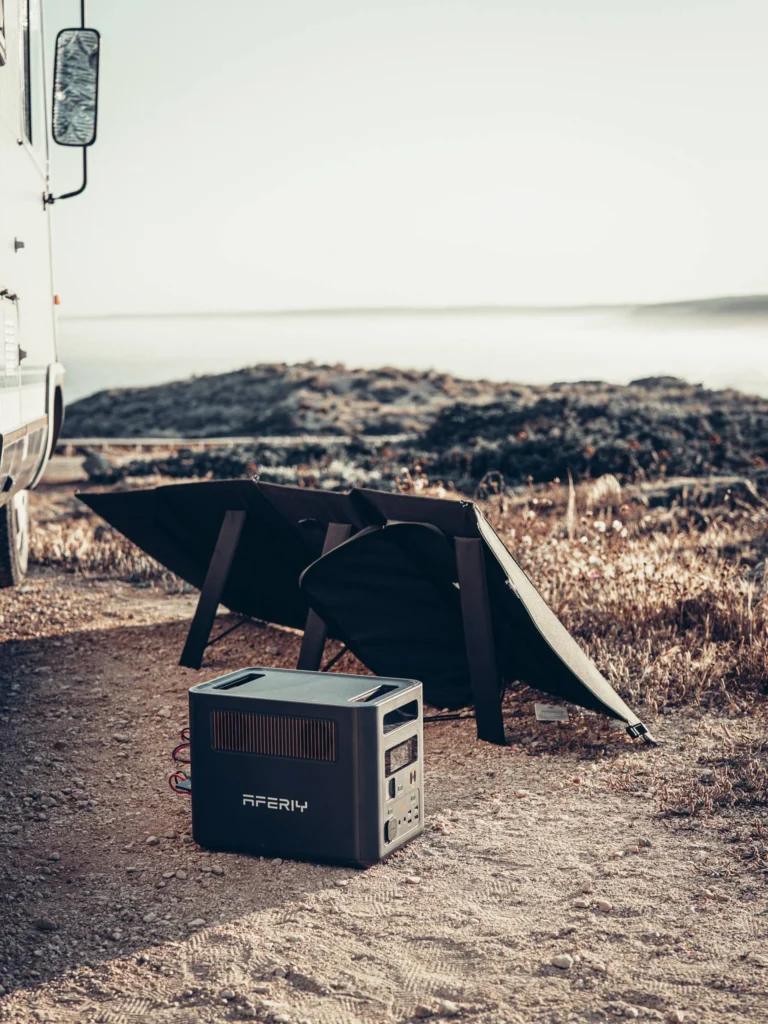 Station Aferiy Nomad 1800 placed on the ground next to an unfolded solar panel near the campervan