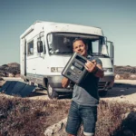 Xavier holding the portable power station Aferiy Nomad 1800 in front of the camper van Édouard, solar panel deployed in the great outdoors
