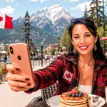 Caroline takes a selfie with a smartphone in front of Canadian mountains, with the Canadian flag in the background.