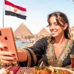 Caroline taking a selfie in front of the Giza pyramids, Egypt, with an Egyptian flag in the background.