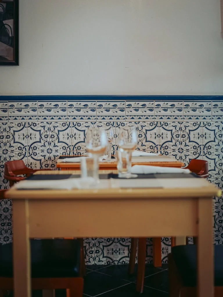 Restaurant table laid with glasses and plates before a wall of traditional azulejos in Tavira, Algarve