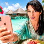Caroline taking a selfie with her smartphone in front of an overwater villa and turquoise lagoon in the Maldives