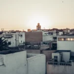 White roofs of the medina of Essaouira at sunset, with the silhouette of a tower in the background.