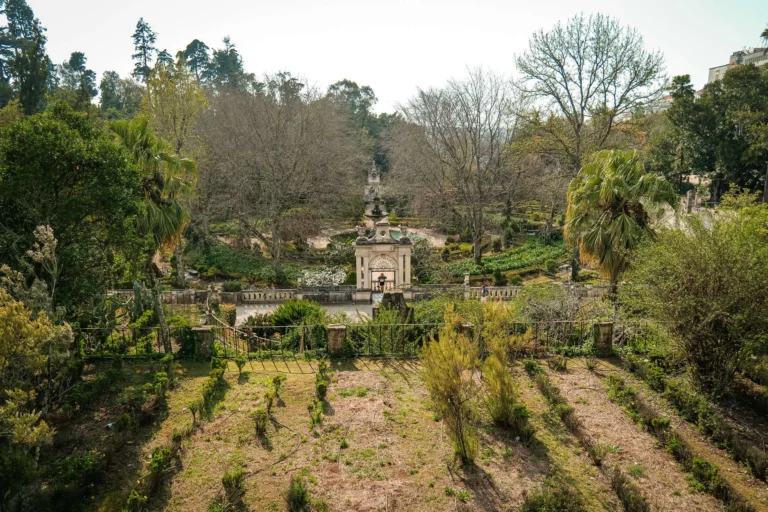 View of the Botanical Garden of Coimbra in early spring, with structured pathways, trees still without leaves, and historical architecture at the center of the park.