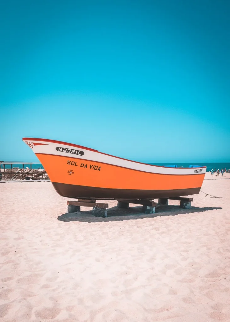 Colorful traditional boat resting on the sand of a beach in Nazaré, under a blue sky in summer.