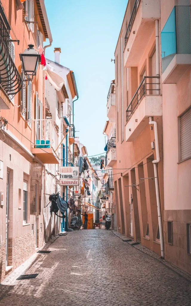 Typical cobbled street of Nazaré in Portugal, lined with colorful houses and balconies with laundry hanging, under a clear sky in summer.
