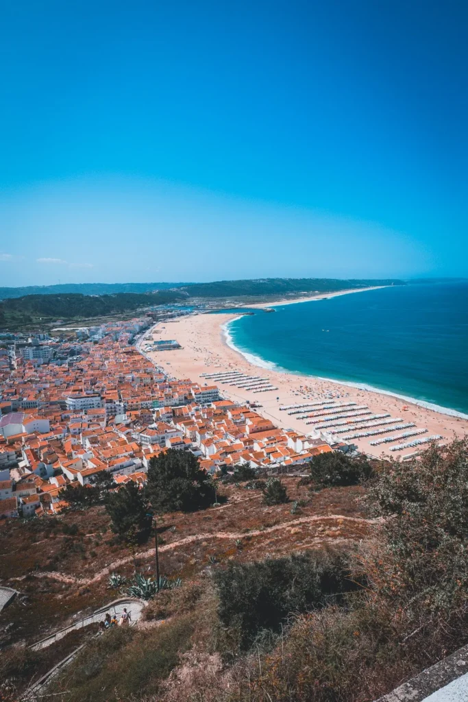 Panoramic view of Nazaré beach and the red roofs of the village, under a blue sky in summer.