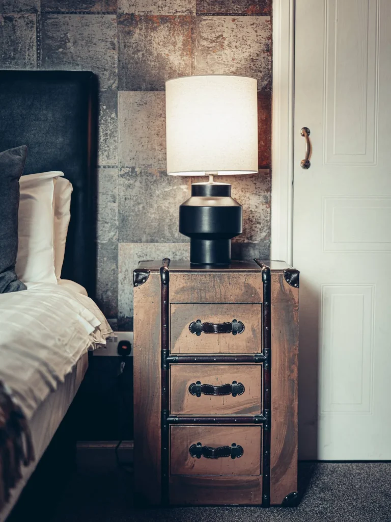 Vintage wooden bedside table with three drawers, topped with a modern lamp, next to a bed in a room at the Allan Park Hotel in Stirling in August 2026.
