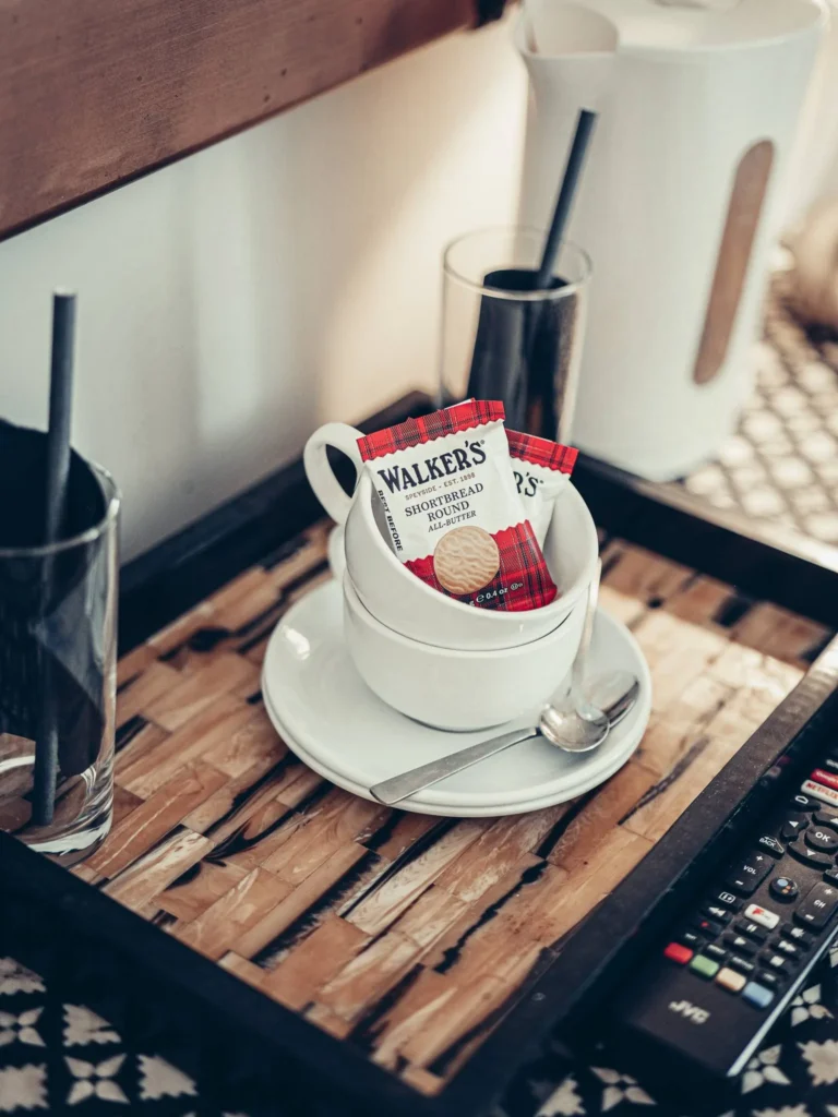 Welcome tray in a room at the Allan Park Hotel in Stirling, with cups, Walkers biscuits, kettle, and remote control on a wooden table.