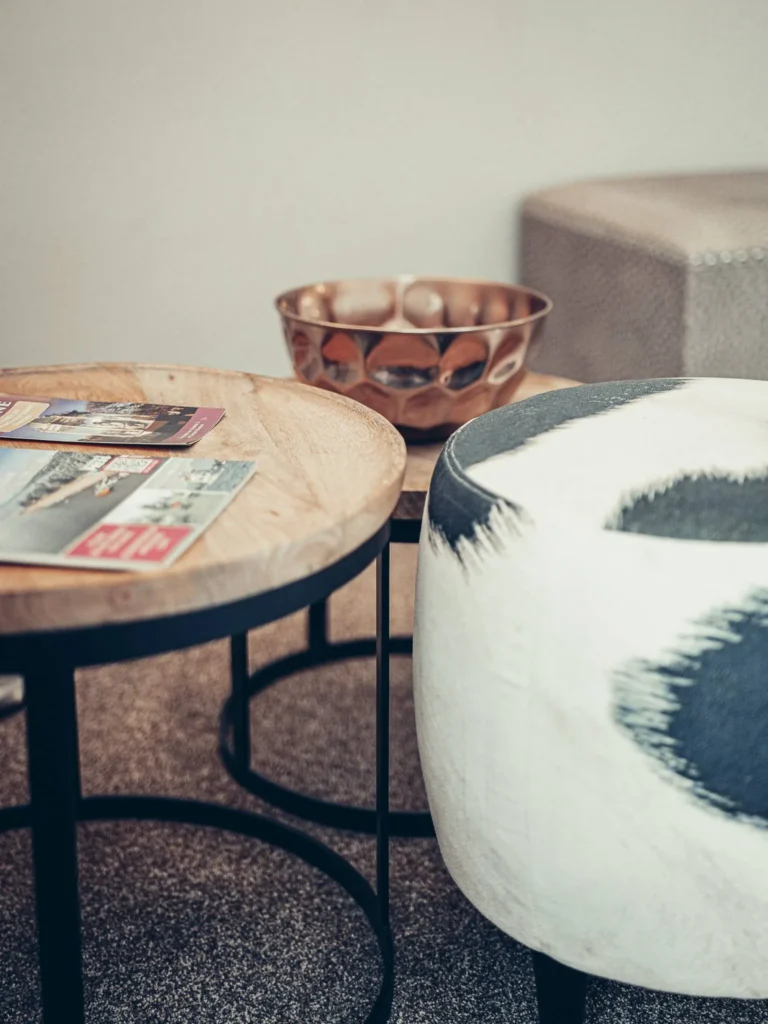 Detail of a lounge area in a room at the Allan Park Hotel in Stirling, featuring a wooden coffee table, a patterned pouf, and a decorative metal bowl.
