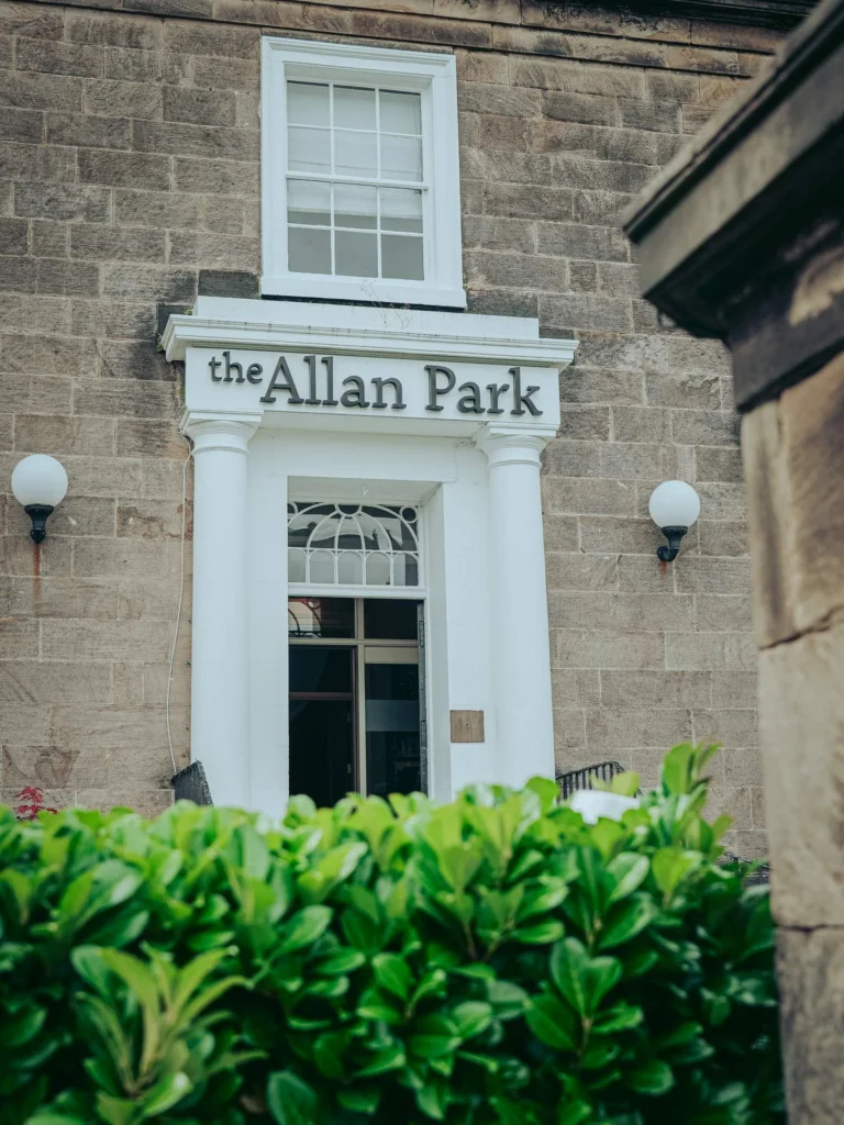 Stone facade of the main entrance of the Allan Park Hotel in Stirling, featuring white columns and a visible sign, taken in summer.