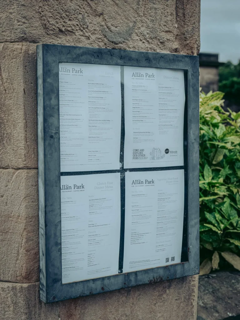 Exterior display of the menus at the Allan Park Hotel in Stirling, on a stone wall with nearby vegetation, in summer 2026.
