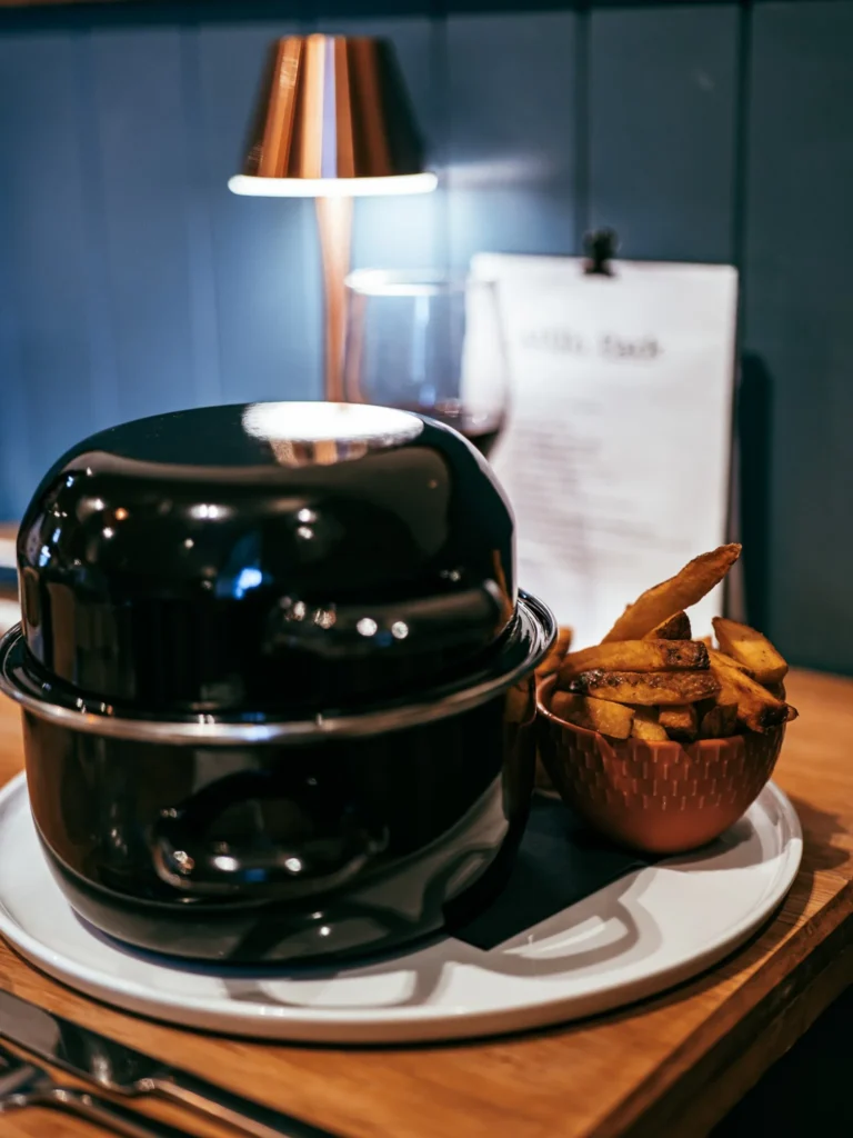 Dish from the Allan Park Hotel restaurant in Stirling, Scotland, served under a black cloche with a portion of homemade fries, on a wooden table illuminated by a designer lamp.