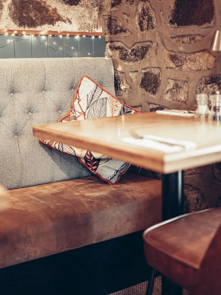 Gray and brown fabric bench with patterned cushion, set table and exposed stone wall in the warm atmosphere of the Allan Park Hotel in Stirling.