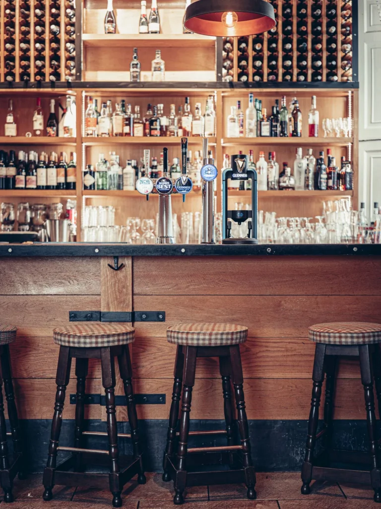 Bar counter of the Allan Park Hotel in Stirling, Scotland, with wooden stools, beer taps, and shelves filled with bottles of alcohol and glasses. Warm atmosphere and wooden decor.