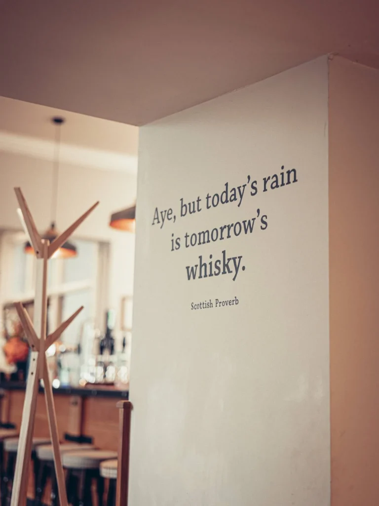 Interior wall of the Allan Park Hotel in Stirling, Scotland, displaying a Scottish proverb about whisky, with a glimpse of the bar in the background.