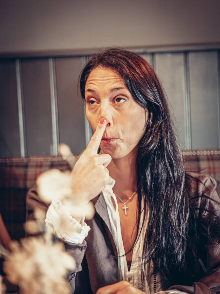 Caroline sitting at a table in the Ben Nevis Bar in Fort William, making a face while touching her nose, relaxed atmosphere in the Scottish Highlands in August.
