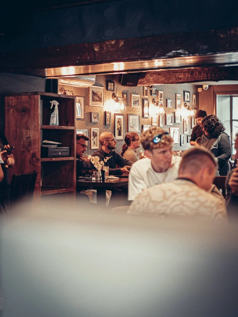 Ben Nevis Bar in Fort William, warm atmosphere with seated customers and frames hanging on the wall, typical dim lighting of the Highlands in summer.