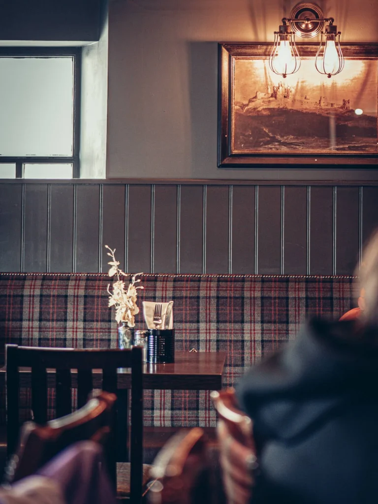 Restaurant table with tartan-patterned bench, dried bouquet and cutlery, warm atmosphere in a Scottish Highlands establishment.