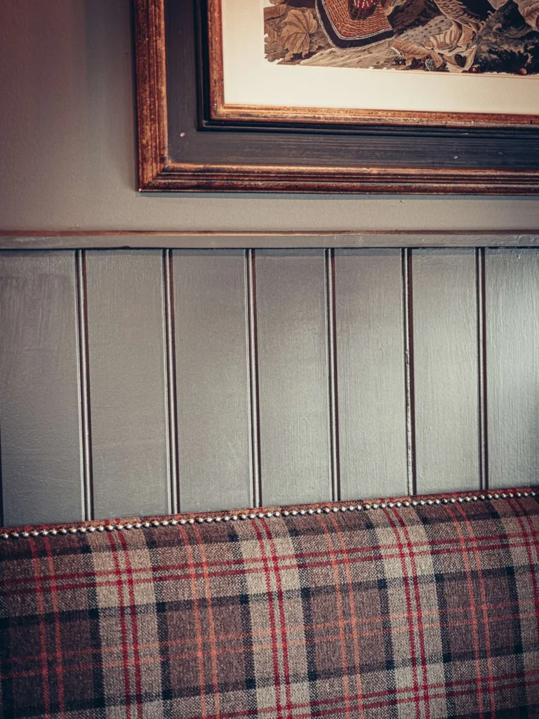 Tartan-patterned bench and grey paneling in a Highlands restaurant, with a framed painting on the wall.