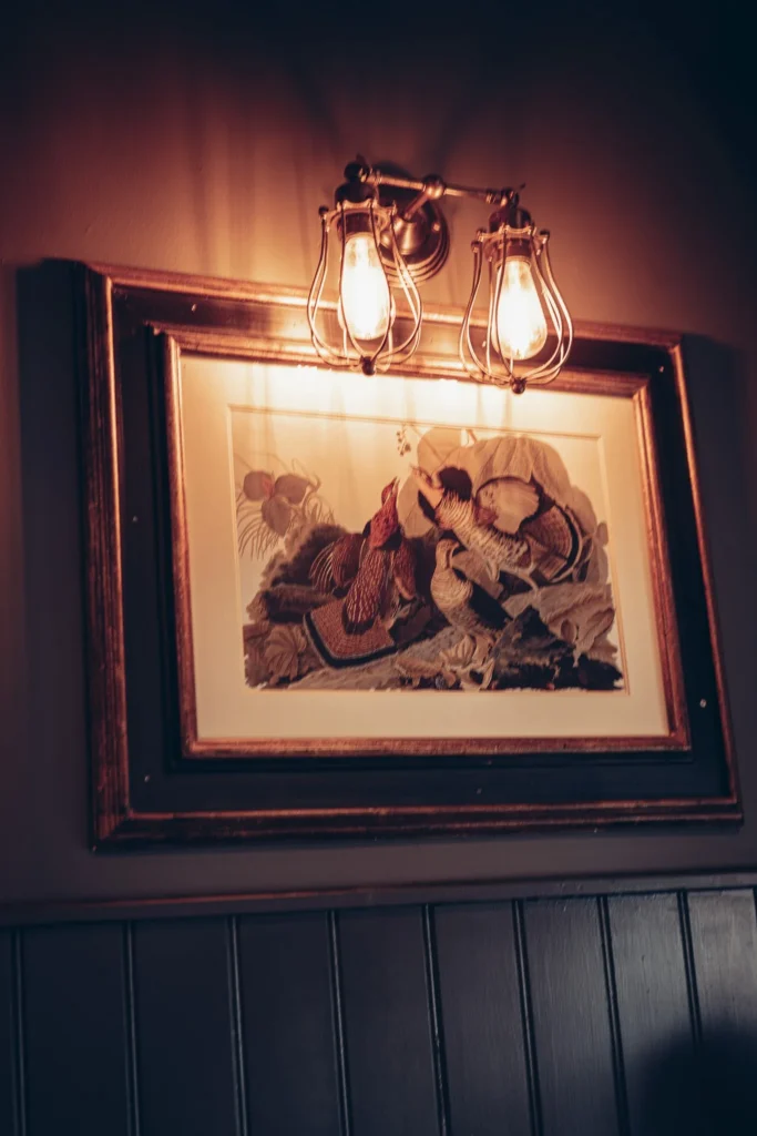 An old frame hanging on a dark wall, illuminated by a vintage wall lamp, in a warm atmosphere typical of a restaurant in the Highlands of Scotland.