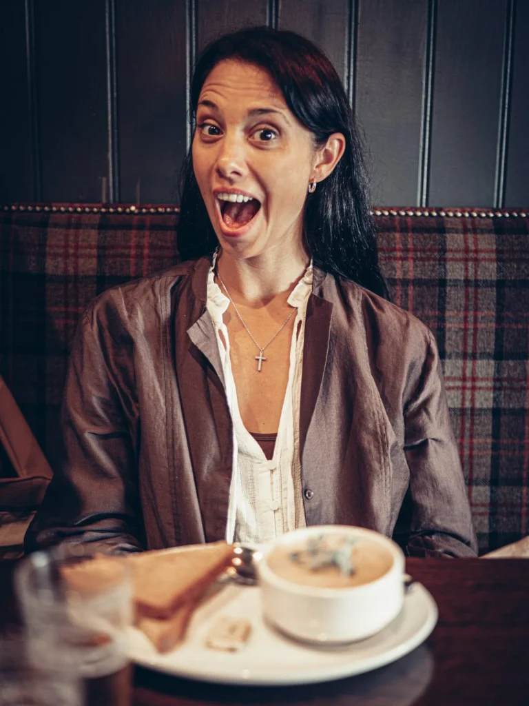 Caroline sitting in Ben Nevis Bar in Fort William, in front of a plate with soup and bread, warm atmosphere of the Scottish Highlands in August.