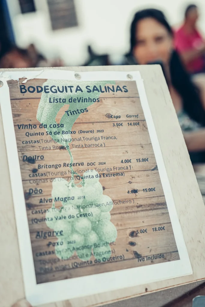 Red wine list from Bodeguita Salinas in Tavira placed on a terrace table: house wine Quinta Sá de Baixo, Douro, Dão, and Algarve, prices by the glass and bottle.