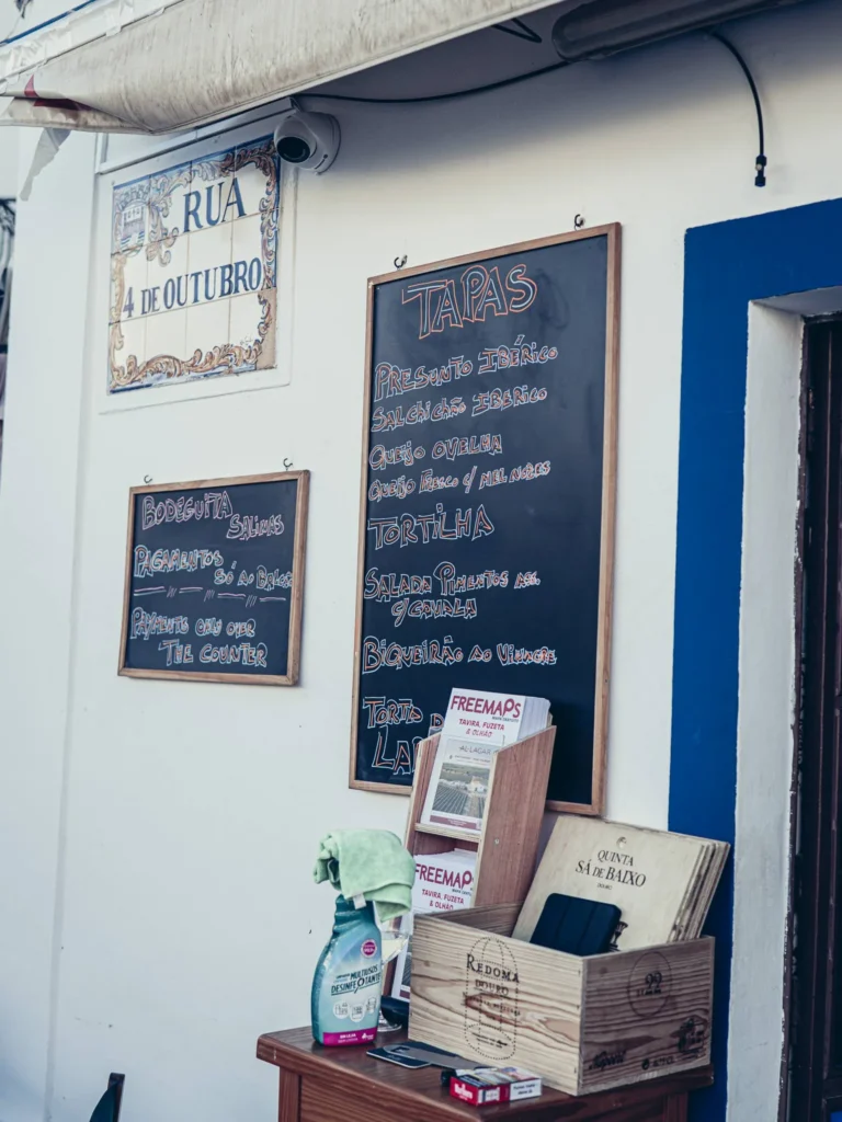 Facade of Bodeguita Salinas, Rua 4 de Outubro in Tavira: wall slates listing the tapas in chalk and wine crates, typical white and blue facade of the Algarve.