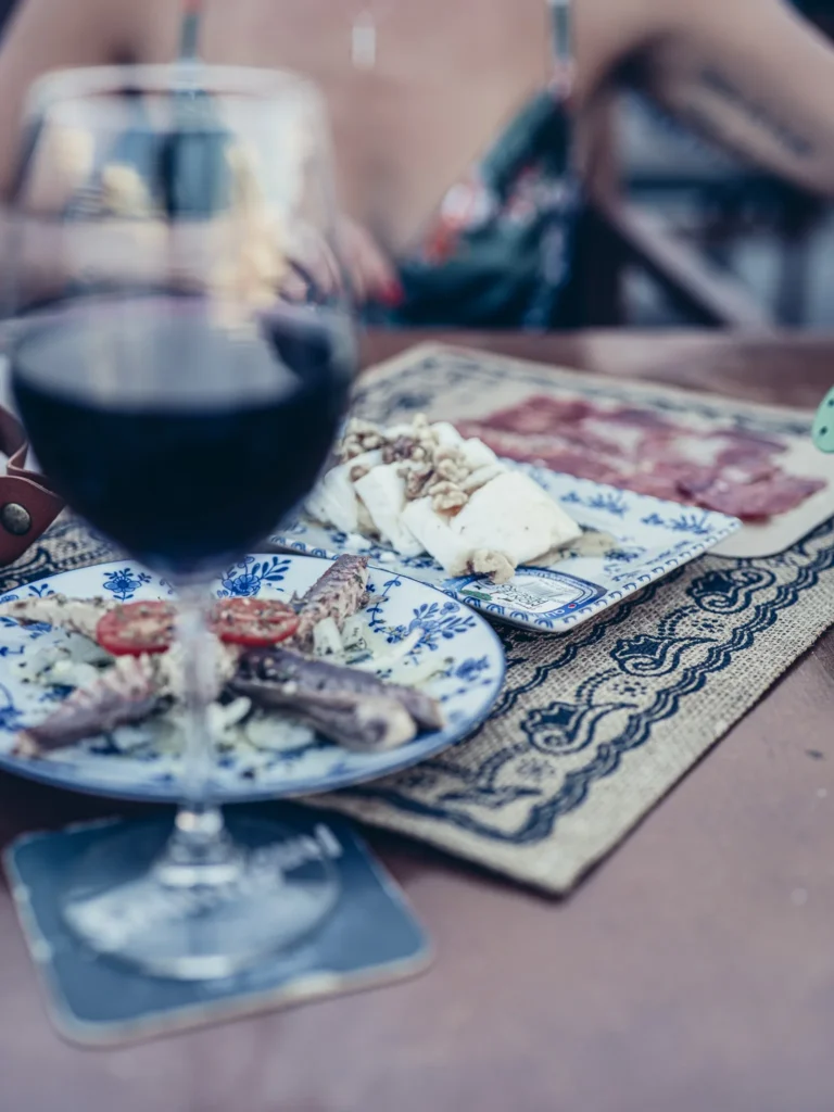 Tapas plate from Bodeguita Salinas in Tavira: cheese, cold cuts, and fish accompanied by a glass of red wine on the terrace table.