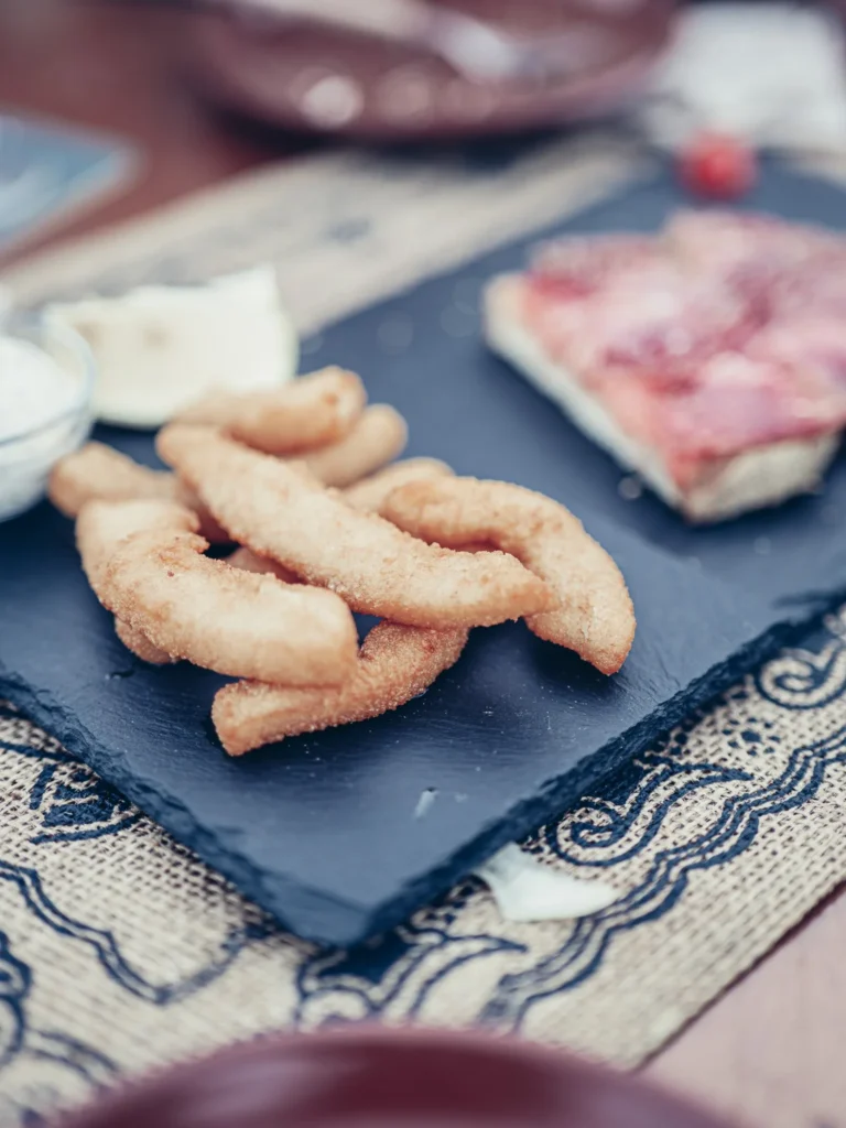 Fried choco strips (cuttlefish fritters) served on a slate with their garlic mayonnaise at Bodeguita Salinas in Tavira, with a slice of Iberian ham in the background.