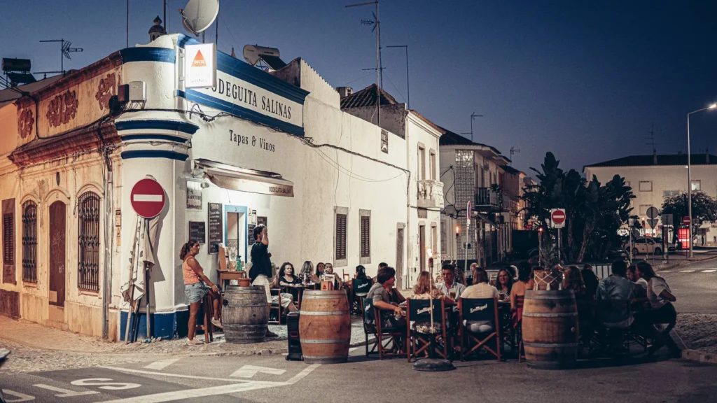 Terrace of the Bodeguita Salinas in Tavira in the evening, groups seated in the street under the urban lighting of the historic center.