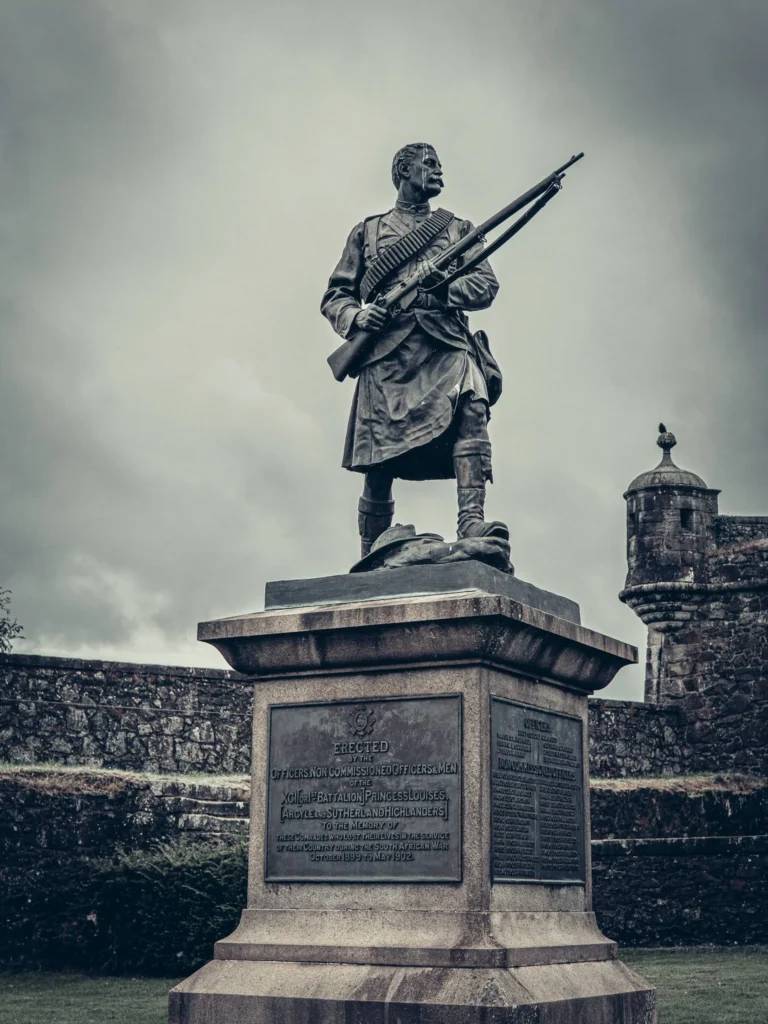A statue of a Scottish soldier in traditional uniform in front of the ramparts of Stirling Castle under a cloudy sky.